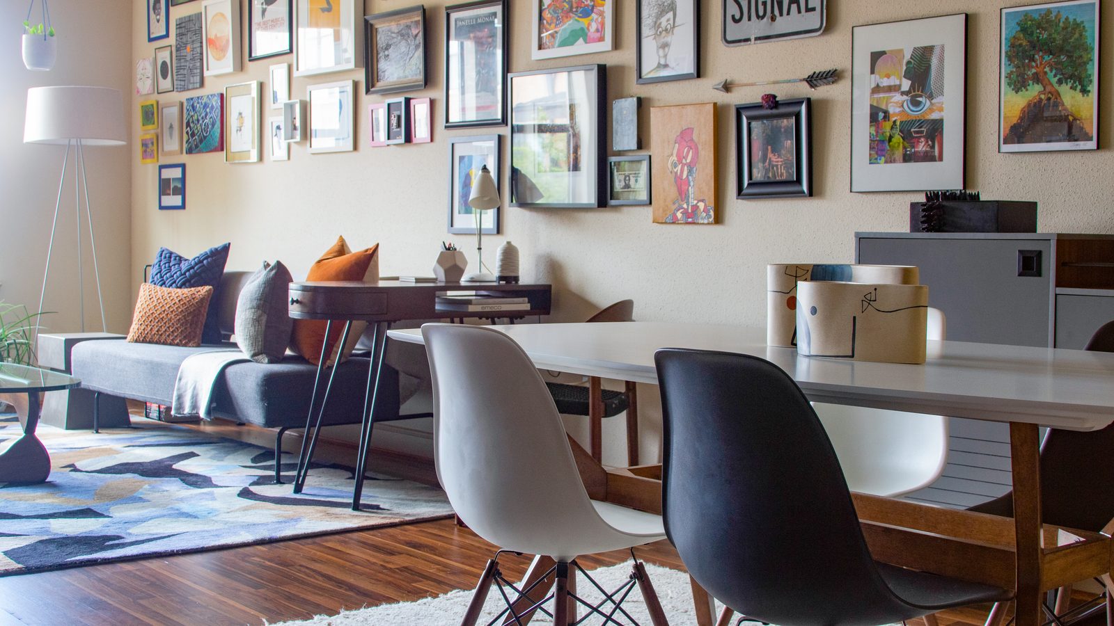 An art-filled open living and dining room with a blue patterned rug, gray sofa and white dining table