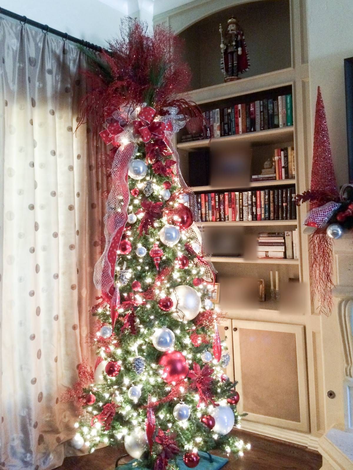 A slim Christmas tree in red, silver and white beside library shelves